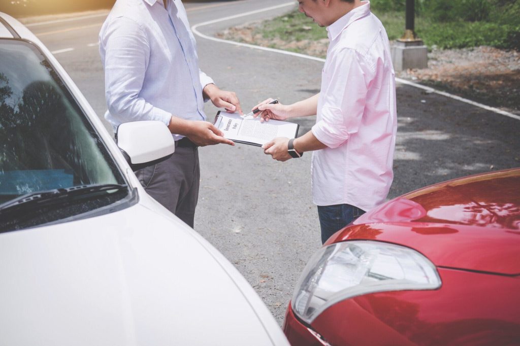 what to do if involved in a car accident - insurance agent examining damages on paper next to car with auto owner
