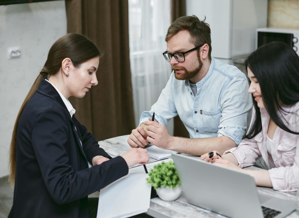 Independant insurance agent helping male and female couple select insurance plan at desk with laptop.
